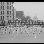 Protesters march at Women's Equal Rights Parade carrying a banner stating "equality of rights under the law shall not be denied or abridged by the united states or any state on account of sex"